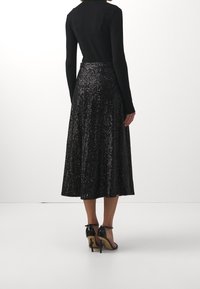 Svart långärmad topp i kombination med en midi kjol täckt av blanka paljetter, med en luftig silhuett och ankelremmar.