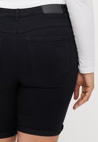 Musta denim-shortsit, joissa on istuva leikkaus, käännetty helma, takataskut ja yksinkertainen vyötärönauhalappu. Sileä kangaspinta.