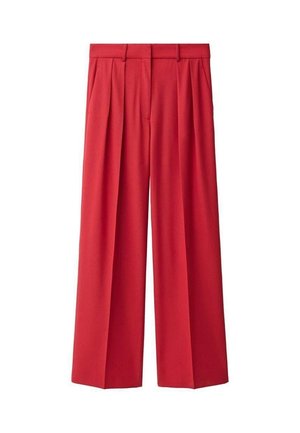 Femme portant un blazer rouge sur mesure à deux boutons et un pantalon plissé taille haute assorti, devant un mur clair uni.