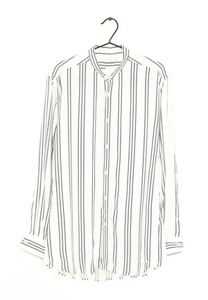 Witte blouse met lange mouwen en verticale zwarte strepen, hangend aan een zwarte hanger tegen een witte achtergrond.