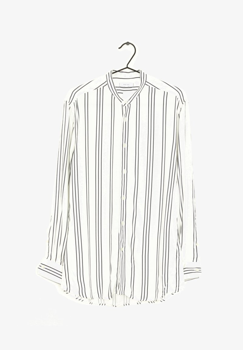 Chemise blanche à manches longues avec des rayures verticales noires, accrochée sur un cintre noir sur fond blanc.