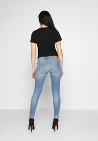 Svart kortärmad t-shirt i kombination med ljusblå skinny jeans med en brun läder-logotyp, bärs tillsammans med svarta klackstövlar.