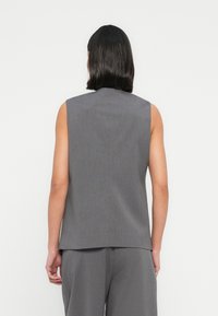 Αμάνικη γκρι μπλούζα με ψηλό λαιμό, κατασκευασμένη από λείο, υφασμάτινο ύφασμα με υφή. Διαθέτει καθαρή σιλουέτα και λεπτομέρεια με άνοιγμα στην πλάτη.