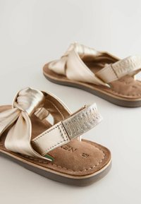 Guldmetalliska sandaler med knuten överdel, vadderad brun mocka fotbädd och texturerade silveraccentband. Flexibel gummisula.