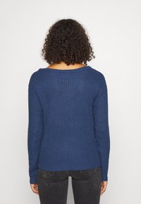 Pull bleu tricoté avec un large col décontracté, une texture côtelée et des manches longues. Design partiellement court avec un ourlet droit.