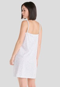 Vestido blanco sin mangas con un patrón floral en azul y rojo. La tela es liviana y fluida, con finas tiras ajustables.