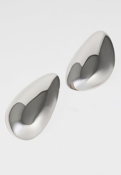 Srebrni kovinski čevlji z gladko, odbojno površino; vsak ima obliko kapljice, z zaobljenimi konci in rahlim ovinkom.