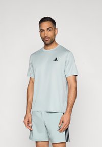 Svetlomodra športna majica s kratkimi rokavi, na levi strani prsnega koša z črnim logotipom; kombinirana z ujemajočimi kratkimi hlačami s črnimi črtami.