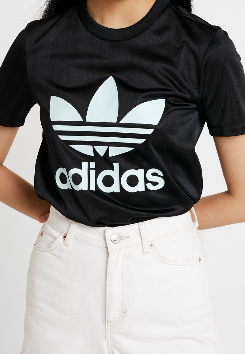 Musta adidas T-paita, jossa on iso vaaleansininen logo ja kolme valkoista raitaa rinnassa. Kangas näyttää sileältä ja kiiltävältä.