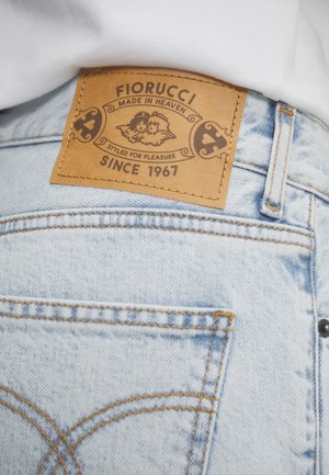 Jeans in denim azzurro chiaro con una toppa marrone del marchio Fiorucci sopra la tasca posteriore, con logo e testo "Made in Heaven, Since 1967."