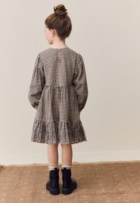 Šaty so vzorom kocky, s dlhými nafúknutými rukávmi a volánovým lemom. Zadná časť má zapínanie na gombíky. Kombinované s čiernymi čižmami a béžovými ponožkami.