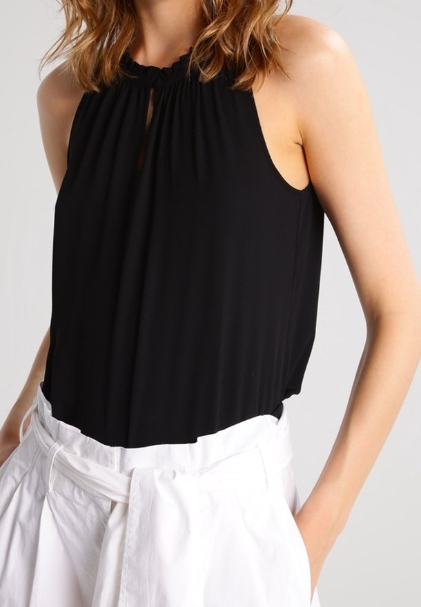 Svart halterneck-top i mjukt tyg, med en nyckelhålsdetalj vid halsen och ärmlös design, kombinerad med vita högmidjade byxor.