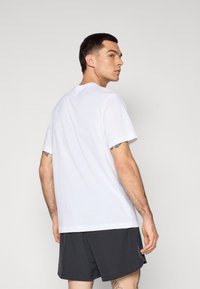 White short-sleeve t-shirt with crew neck, made of a smooth fabric; worn with dark shorts, showcasing a simple, classic design.