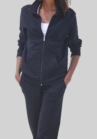 Black zip-up hoodie with a high collar, front pockets, and ribbed cuffs; paired with matching joggers, made of soft, stretchy fabric.
