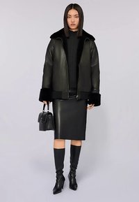 Černá kožená bunda s kožíškovým límcem, černý pletený svetr, kožená tužková sukně, černé kozačky po kolena a malá černá kabelka.