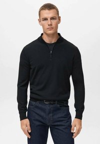 Schwarzer Strickpullover mit Reißverschlusskragen, langen Ärmeln und taillierter Passform. Getragen mit einer dunklen Jeans und einem geflochtenen Gürtel, was einen lässigen Look betont.