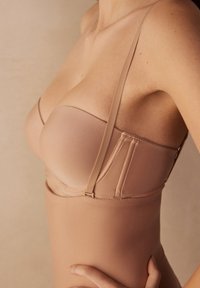 Naadloze naakte bh met dunne bandjes, een gladde textuur en gevormde cups. Voorzien van beugel en haaksluitingen aan de zijkant.