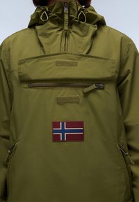 Grüne Nylonjacke mit einem halben Reißverschluss, verfügt über eine zentrale Tasche, einen Seitenreißverschluss und ein Patch der norwegischen Flagge. Glatte Textur.