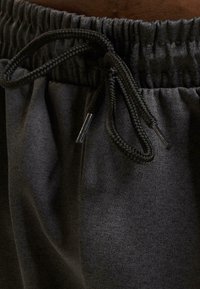 Grå sweatpants med en elastisk talje, der har en snøre med metalspidser, og et blødt, struktureret stof.