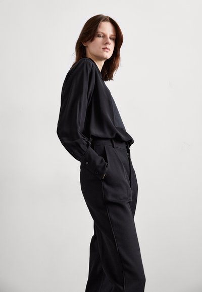 Black long-sleeve blouse paired with high-waisted black trousers. The fabric appears smooth with a relaxed fit and minimal stitching details.