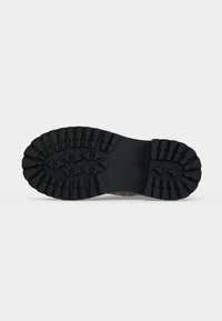 Semelle de botte en caoutchouc noir avec des crampons profonds et robustes présentant des motifs triangulaires et rectangulaires pour une forte adhérence et durabilité.