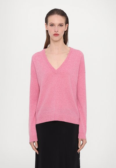 Un pull rose à col en V avec des manches longues, à la texture douce et à la coupe décontractée, associé à une jupe noire, au design minimaliste et sans motifs visibles.