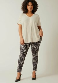 Lys beige V-hals top med struktureret overflade, parret med tætsiddende leopardmønstrede bukser i nuancer af sort, creme og mauve. Sorte høje hæle.