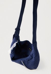 Tumesinine kangast õlakott tekstureeritud pinnaga, tõmblukuga ja sisemise taskuga. Tõmblukule on kinnitatud dekoratiivne tutike.