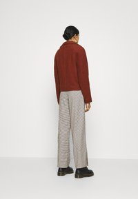 Giacca testurizzata color ruggine con colletto, indossata sopra pantaloni grigio e bianco a fantasia houndstooth e stivali neri con zeppa.