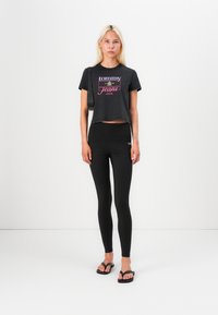 Juodas trumpas T-shirt su spalvingu "tommy jeans" logotipu, derinamas su aukštu liemeniu juodomis kelnėmis ir juodais šlepetėmis.