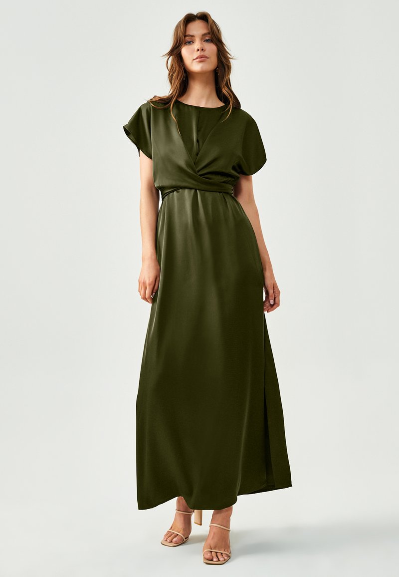 Olivno zelena maxi obleka z ovito zasnovo, kratkimi rokavi in razporkom. Narejena je iz gladkega materiala in ima prilagojen pas.