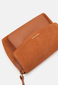 Brun læder- og ruskinds-clutch med en glat tekstur, udstyret med et guld logo og en klaplukning. Pyntet med en aftagelig rem.