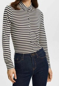 Camicia a righe con maniche lunghe in crema e navy con colletto a punta, dotata di bottoni frontali, abbinata a jeans blu scuro.
