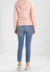 Różowa kurtka z wkładkami, z poziomym przeszyciem, kapturem i dwoma bocznymi kieszeniami. Noszona z dopasowanymi niebieskimi dżinsami i białymi sneakersami.