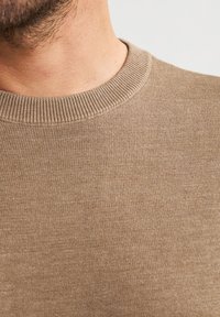 Maglione beige con scollatura a girocollo a coste, texture liscia e silhouette aderente, caratterizzato da un motivo a maglia fine e un colore uniforme.