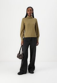 Pull à col roulé vert olive avec des manches ballons, associé à un jean évasé noir taille haute. Sac à main marron avec une bandoulière. Chaussures noires.