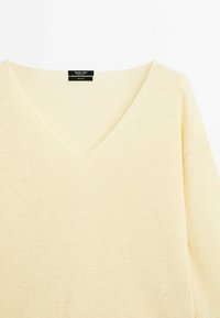 Maglione a V in morbido tessuto a maglia leggero, di colore giallo pallido e con maniche lunghe a vestibilità ampia. Etichetta del marchio visibile al collo.