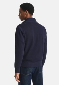 Sudadera azul marino con cuello alto, puños de canalé y tela suave. La vista trasera muestra hombros sin costuras y una cinturilla. 