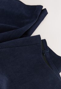 Tissu côtelé bleu marine à texture douce, présentant un ourlet roulé et des bords cousus. Le design comprend un détail de couture cachée.