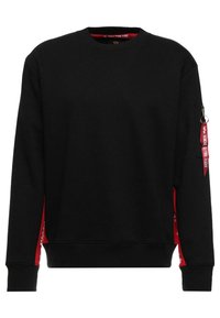 Svart långärmad sweatshirt med röd dragkedjeficka på vänster ärm och röda tygdetaljer längs sidorna och insidan av kragen.