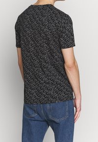 Sort T-shirt med et geometrisk hvidt mønster, korte ærmer, rund hals og en afslappet pasform. Stoffet ser glat ud med en let stræk.