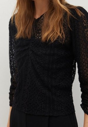 Black lace top features long sleeves, a textured pattern, and gathers at the front. Designed with a v-neckline and fitted silhouette.