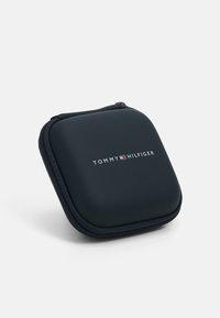 Tommy Hilfiger svart hard case med jevn tekstur, firkantet form og kontrasterende hvit logo sentrert på fronten. Glidelåslukking.