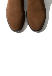 Par smeđih antilop čizama s zaobljenim vrhovima i crnim gumenim potplatima na bijeloj pozadini.