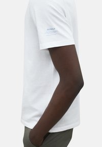 Camiseta blanca de algodón de manga corta, con el logo de Ecoalf en azul en el brazo izquierdo. Textura suave, corte estándar, diseño simple.