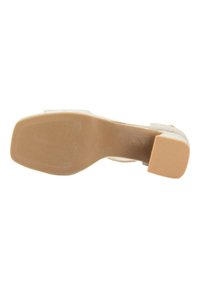 Zapato de tacón alto beige con parte superior suave, punta redondeada y suela de goma texturizada. El tacón mide aproximadamente 5 cm de altura.