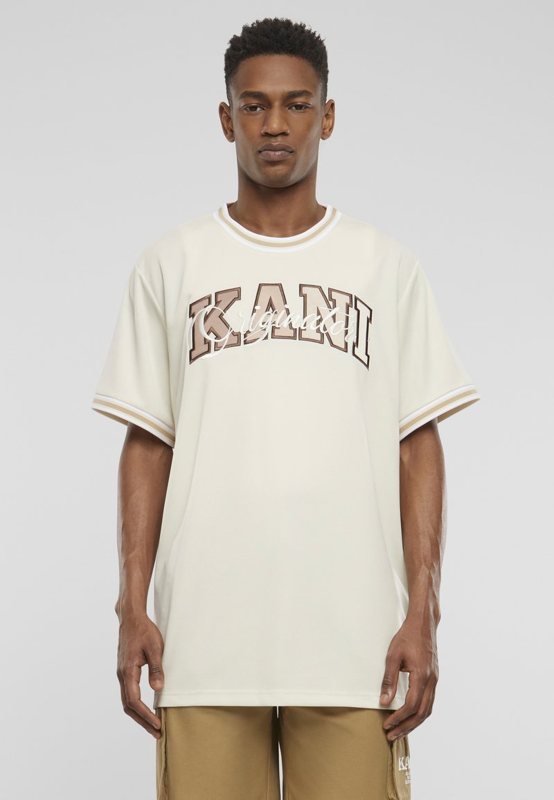 Cremefarvet oversized t-shirt med ribbet hals og brun skrift "KANI" tværs over brystet. Korte ærmer har hvide accenter.