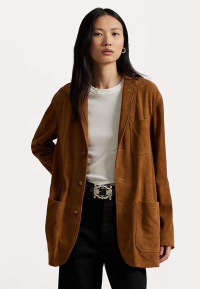 Brauner Wildleder-Blazer in lässiger Passform, mit vorderen Knöpfen, einer Brusttasche und zwei großen Vordertaschen. Kombiniert mit einem weißen T-Shirt.