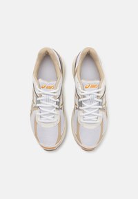 Pair of white ASICS sneakers with beige accents and orange logo, viewed from above on a plain white background.