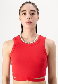 Piros bordázott crop top, kerek nyakkivágással és ujjak nélkül. Különleges csomózott díszítéssel a deréknál, rugalmas anyagból készült.